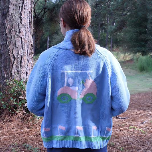 Person wearing a blue sweater with a golf cart design outdoors