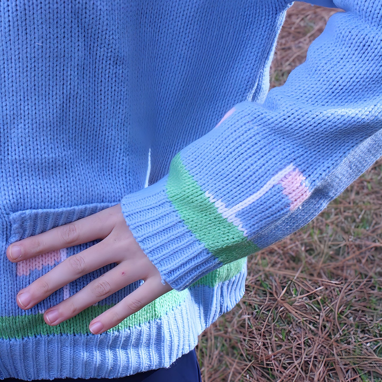 Person wearing a blue sweater with a colorful pattern on the sleeve, standing outdoors.